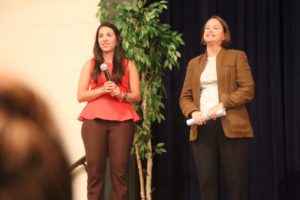 TIRRC's Camila Fyler and Attorney Bethany Jackson with Justice For Our Neighbors standing on stage with a microphone