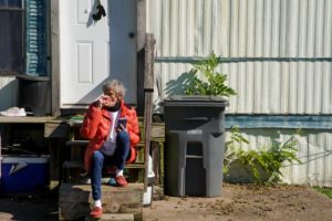woman sits in front of mobile home smoking cigarette