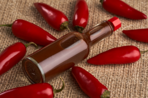 A bottle of hot sauce surrounded by red peppers.