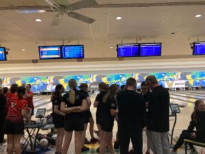 Members of Vanderbilt Women's Bowling huddle in front of open bowling lanes.