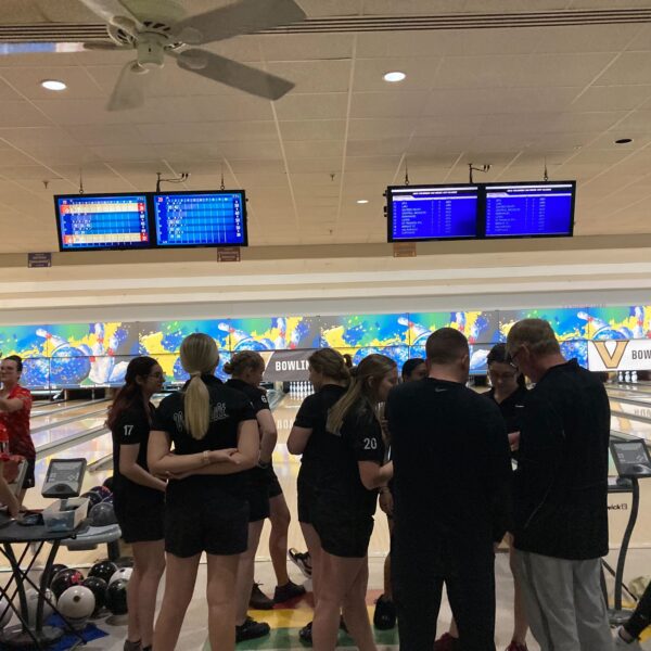 Members of Vanderbilt Women's Bowling huddle in front of open bowling lanes.