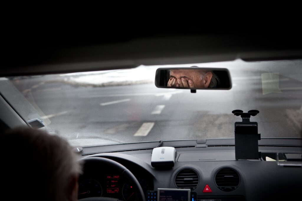 Man rubs his eyes in frustration while he's behind the driver's seat of a car.