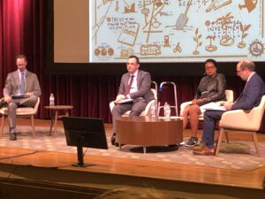 Mayor Freddie O'Connell (left), meets with the chairs of his three transition committees, (left to right) Alex Jahangir, Christy Pruitt-Haynes, and David Esquivel. They chair "How Nashville Moves," "Works," and "Grows," respectively. They sit in white armchairs on a stage with a colorful flowchart projected above them.