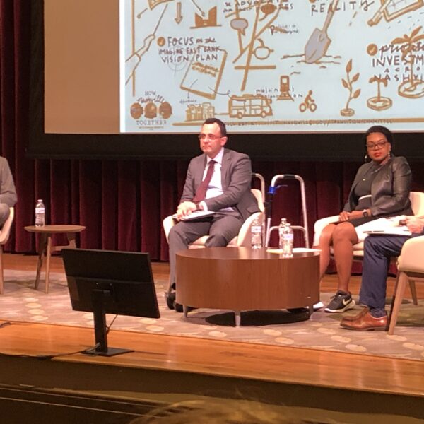 Mayor Freddie O'Connell (left), meets with the chairs of his three transition committees, (left to right) Alex Jahangir, Christy Pruitt-Haynes, and David Esquivel. They chair "How Nashville Moves," "Works," and "Grows," respectively. They sit in white armchairs on a stage with a colorful flowchart projected above them.