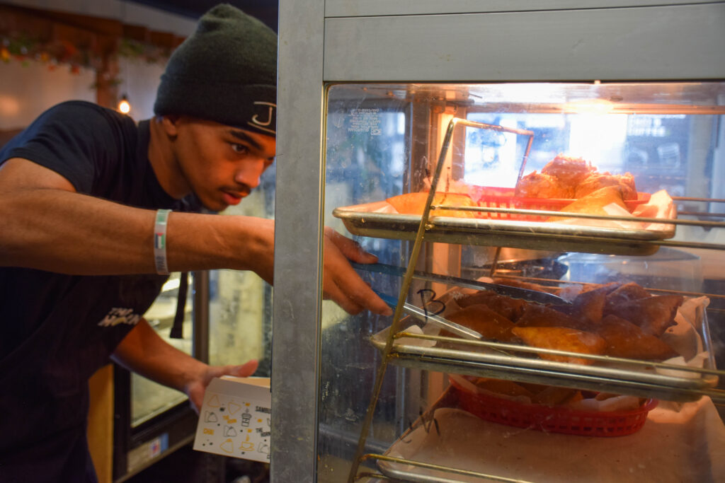 A Horn Coffee employee grabs a sambusa out of a glass case using tongs.