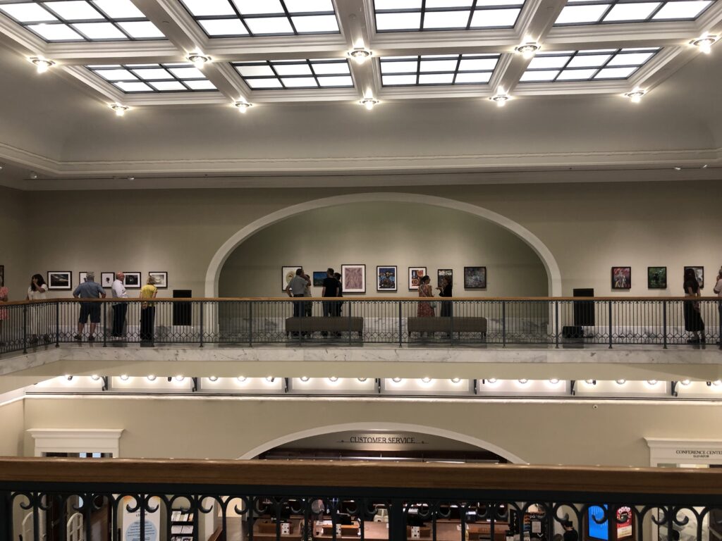 An ornate art gallery on a balcony, with paintings displayed in large nooks with sloped ceilings.