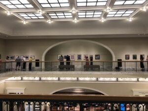 An ornate art gallery on a balcony, with paintings displayed in large nooks with sloped ceilings.