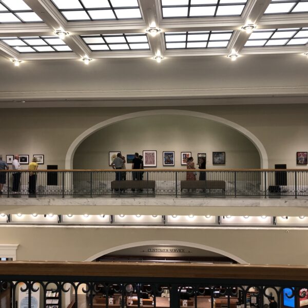 An ornate art gallery on a balcony, with paintings displayed in large nooks with sloped ceilings.