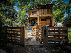 A large dwelling made out of plywood with a fence, two stories, and a garage.