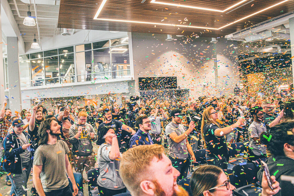 Rainbow confetti falls on a group of cheering students in an atrium.