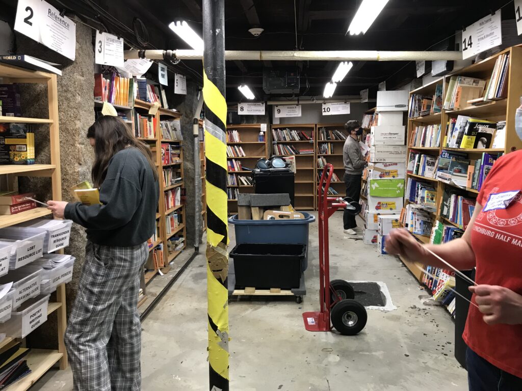 Three people wearing face masks peruse bookshelves in a basement.