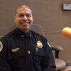 A man in a police uniform with a shaved head sits behind a microphone in a radio studio.