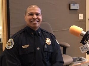 A man in a police uniform with a shaved head sits behind a microphone in a radio studio.