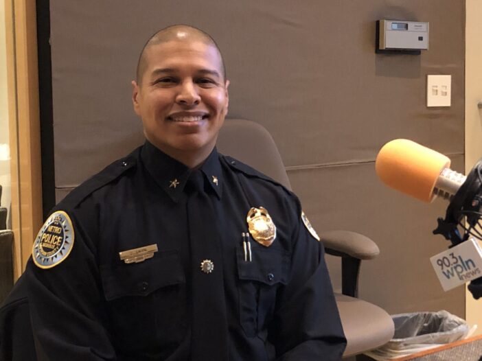 A man in a police uniform with a shaved head sits behind a microphone in a radio studio.