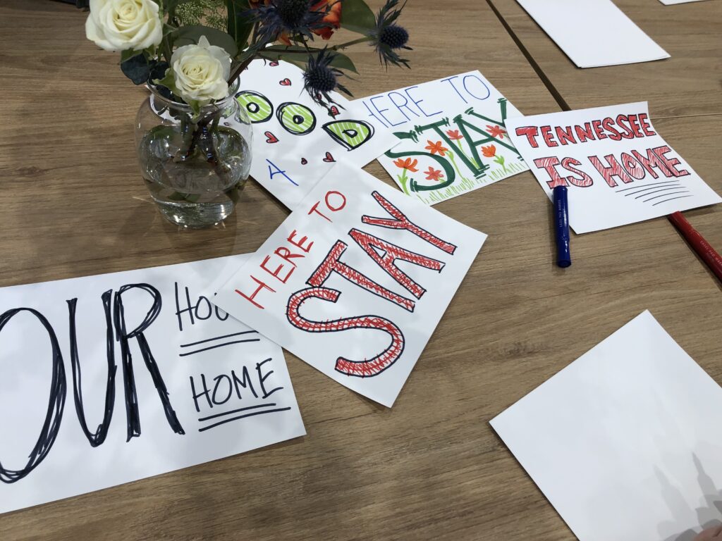 A pile of pro-immigration paper signs on a meeting room table with a small vase of white flowers in the center.