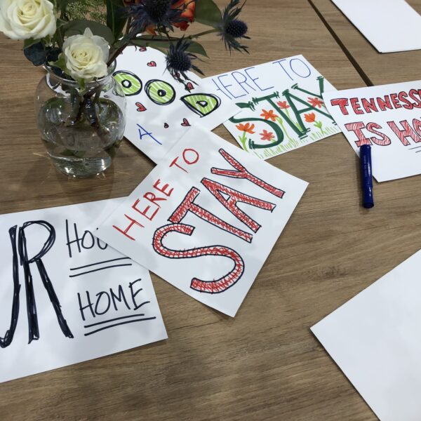 A pile of pro-immigration paper signs on a meeting room table with a small vase of white flowers in the center.