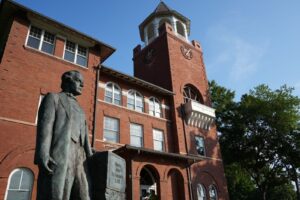 A statue of a man stands in front of a historic three-story brick courthourse.