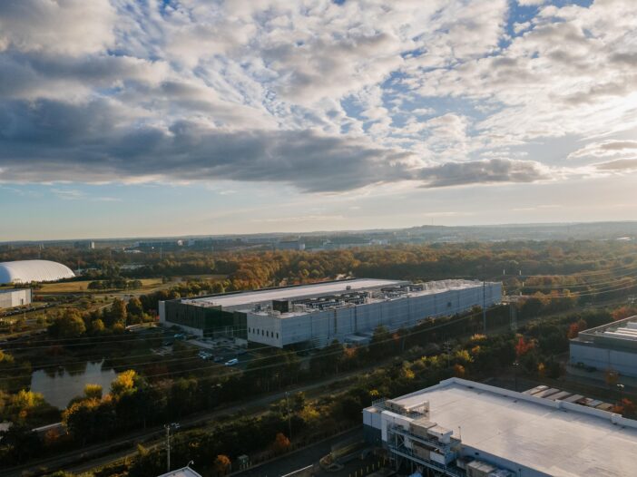 This photo taken from high above shows a Meta data center in Ashburn, Virginia, in 2025. It is a large, long light-colored building with few windows, and it's nestled among trees and a few other buildings with a similar shape.