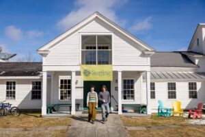 Izzy Johnson, left, and Jack Beatson are first-year students at Sterling College in Craftsbury Common, Vermont. The two students are walking out of the college building into the yard.