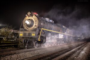 A steam locomotive is surrounded by fog at night.