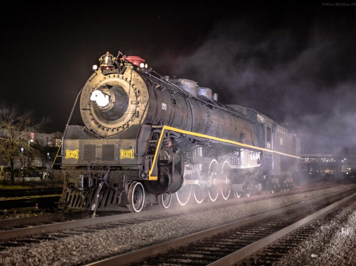 A steam locomotive is surrounded by fog at night.