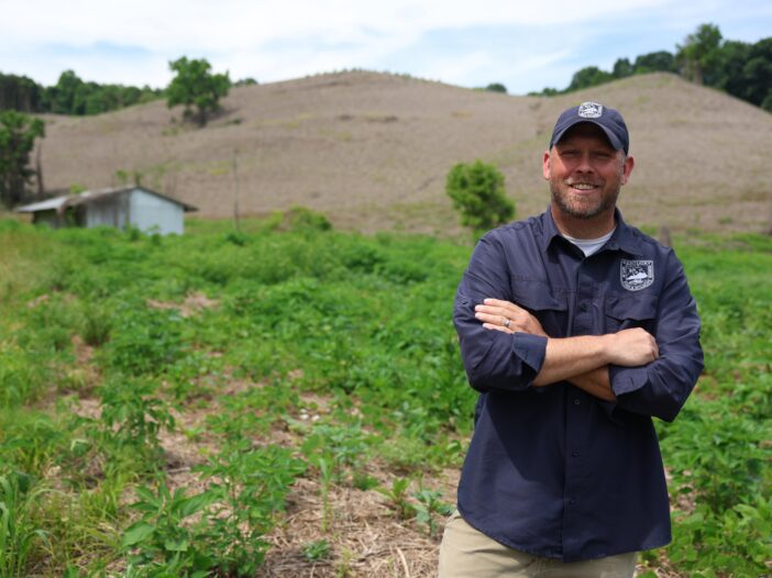 Jacob Stewart, Private Lands Program coordinator for Kentucky Fish and Wildlife Resources, poses before a hillside in Whitley County covered in dying kudzu. Around him, native plants and fauna choked out by the vine have already sprouted in its place. The 26-acre property once housed a coal mining operation and was one of eight sites statewide where the new treatment was studied.