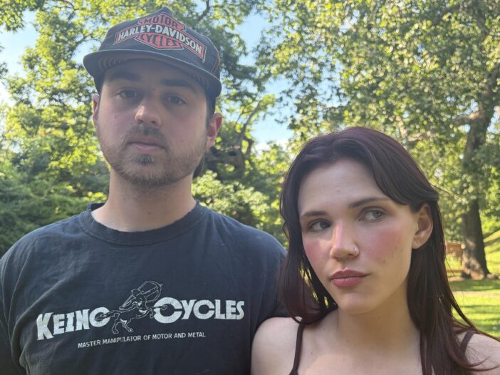 In this photo, Chloe Troub stands on the right side of the frame, and her boyfriend, Carson McDonald, is standing on the left side of the frame. Standing outdoors, they are photographed from about the shoulders up, and trees are in the background.
