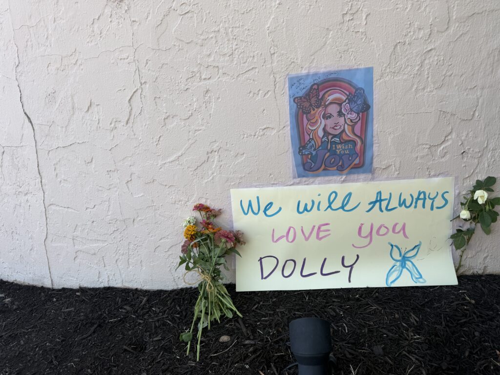 Close up photo of a tribute of flowers and signage left by a Dolly Parton fan at a small wall mural in Nashville, TN.