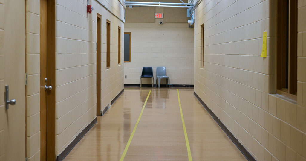 Two chairs sit empty at the end of a long hallway in an industrial-looking building.