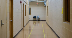Two chairs sit empty at the end of a long hallway in an industrial-looking building.