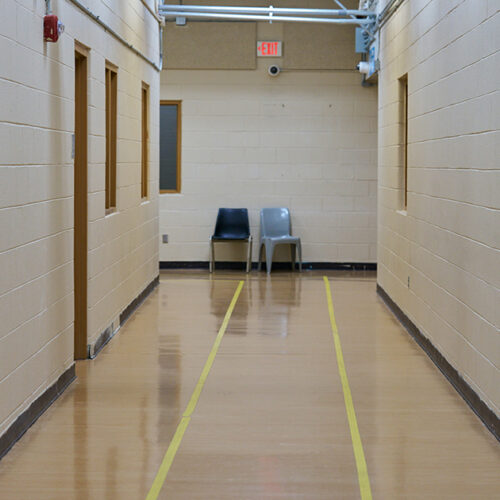 Two chairs sit empty at the end of a long hallway in an industrial-looking building.