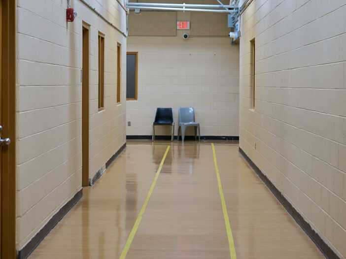 Two chairs sit empty at the end of a long hallway in an industrial-looking building.