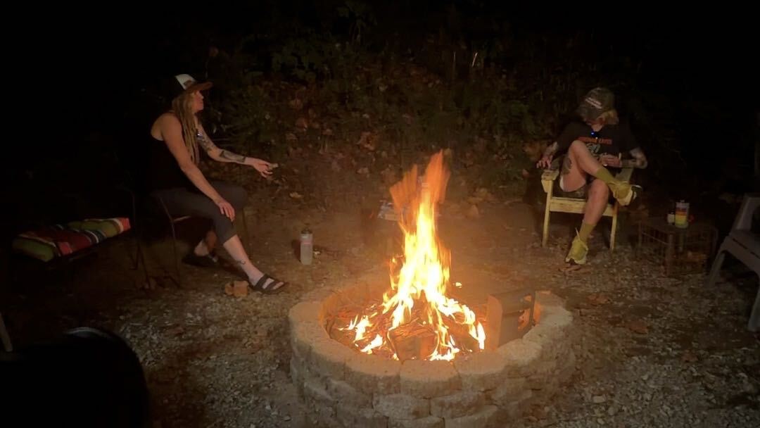 Two people sit around a campfire.