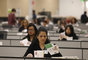 Election workers who are seated and wearing clear gloves process ballots for the California state primary.