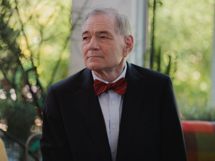 Retired Judge David Duncan poses for a photo while seated at his home in Phoenix. He is wearing a dark suit and a red bow tie with thin navy blue and marigold stripes.